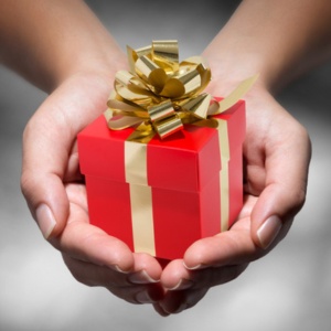 Les mains tiennent un petit paquet cadeau rouge avec un ruban et un nœud dorés.