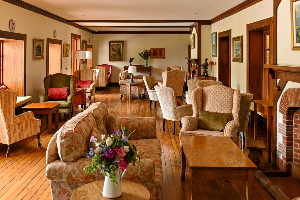 Die geräumige Lounge des Renvyle House ist mit gemusterten Sesseln, Sofas, Holztischen, einem Kamin, Blumenarrangements und gerahmten Gemälden an cremefarbenen Wänden mit hölzernen Akzenten ausgestattet - ein Markenzeichen der 4-Sterne-Hotels in Connemara.