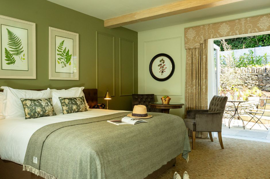 Un letto d'albergo ben fatto con accenti verdi, un tavolino con due sedie e una porta aperta che conduce al patio del giardino di un incantevole hotel a 4 stelle in Irlanda.