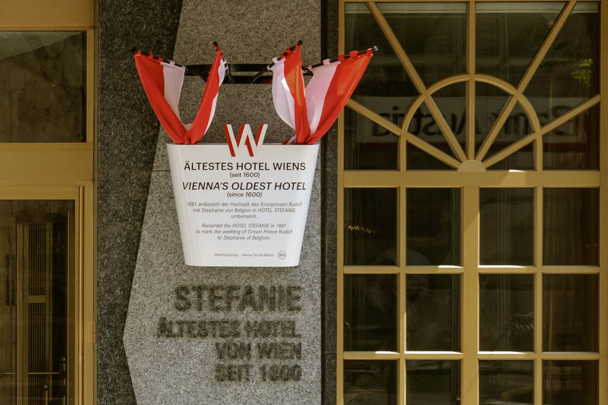 Plaque on a stone facade marks Vienna's oldest hotel, Hotel Stefanie, a 4 star hotel in Vienna city centre established in 1600; red and white flags are displayed above the sign.