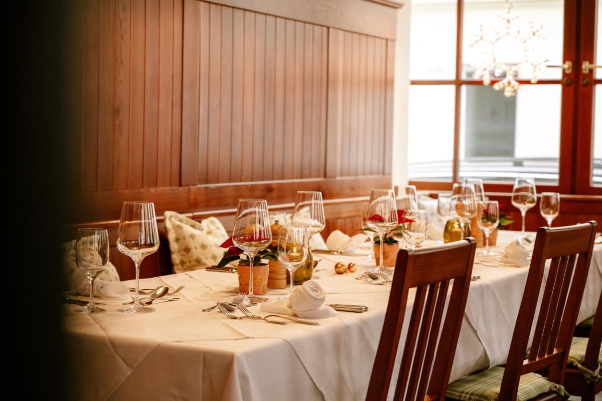 A dining table set for a meal with wine glasses, folded napkins, and cutlery, surrounded by wooden chairs in a warmly lit restaurant at Hotel Erzherzog Rainer in the heart of Wien.