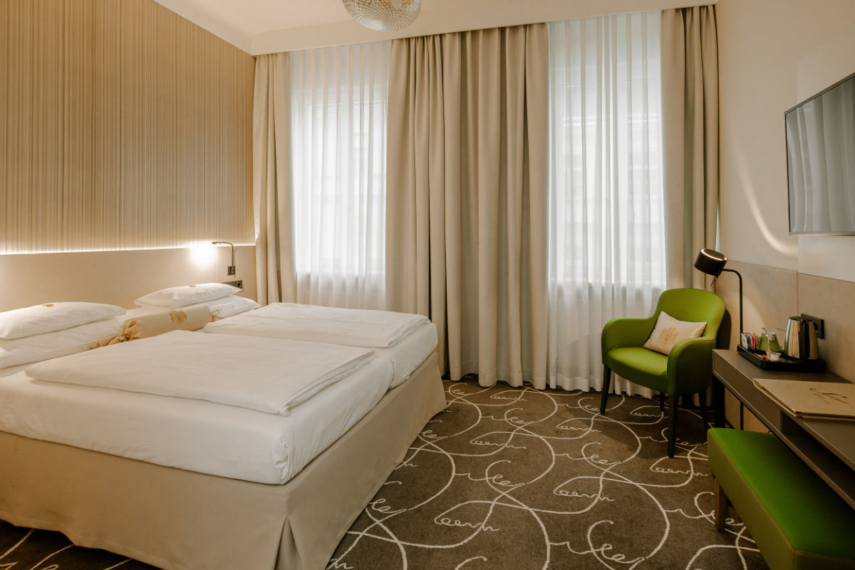 Benvenuti all'Hotel Erzherzog Rainer, dove la vostra camera dispone di due letti, una sedia verde e una scrivania con lampada. Rilassatevi guardando la TV a parete. Le tende beige adornano le finestre e completano il tappeto a motivi circolari per un soggiorno sereno.