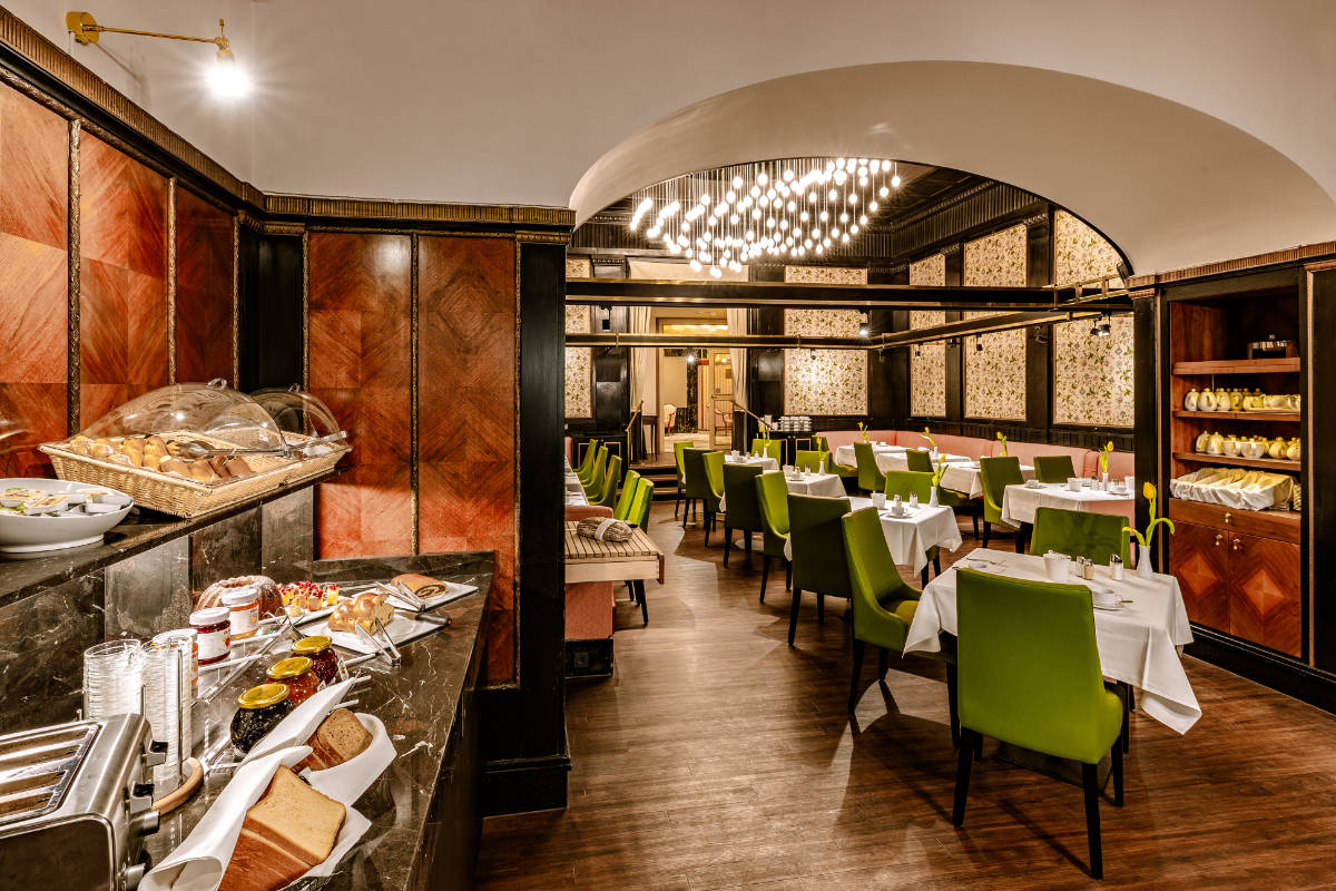 L'elegante interno del ristorante dell'Hotel Erzherzog Rainer è caratterizzato da sedie verdi e tovaglie bianche. Un buffet con pane e condimenti attende sul bancone di marmo, illuminato da un'illuminazione a soffitto con lampadine a sospensione multiple.