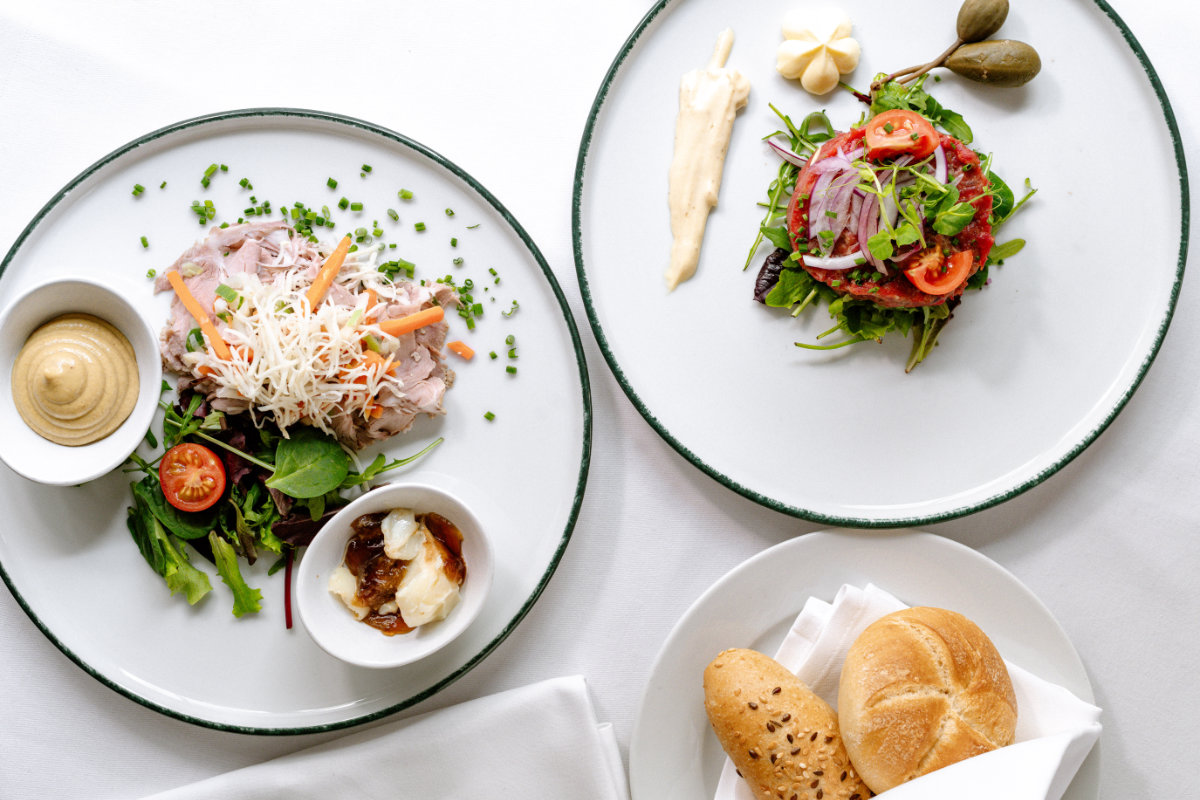 Due piatti bianchi con antipasti gourmet assortiti, tra cui carni, verdure fresche, affettati e salse. Il tutto disposto elegantemente su una tovaglia bianca all'Hotel Erzherzog Rainer.