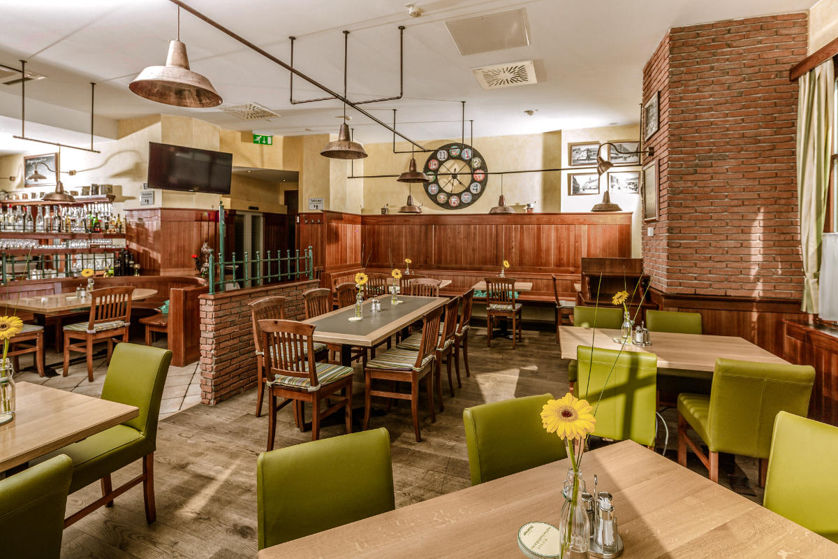 L'accogliente ristorante dell'Hotel Erzherzog Rainer è caratterizzato da tavoli in legno, sedie verdi e affascinanti accenti in mattoni. I girasoli in vaso aggiungono un tocco di allegria a ogni tavolo, mentre un grande orologio adorna elegantemente la parete.