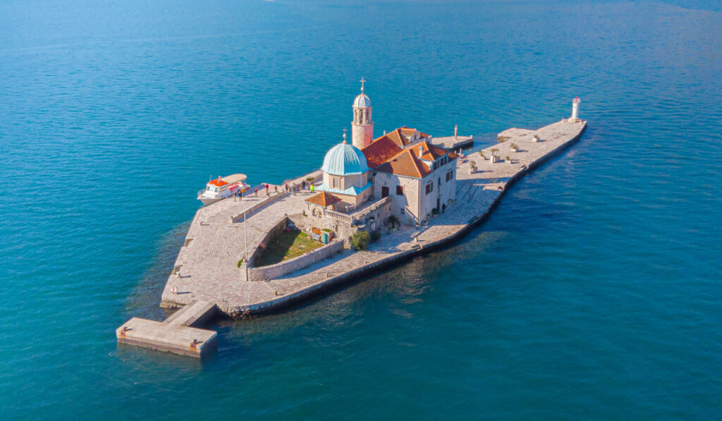 Europe’s Best-Kept Secrets: Lesser-Known Historic Hotel Escapes 16 A small island in Kotor Bay, Montenegro, with the Island Church of Our Lady of the Rocks in the middle of the water.