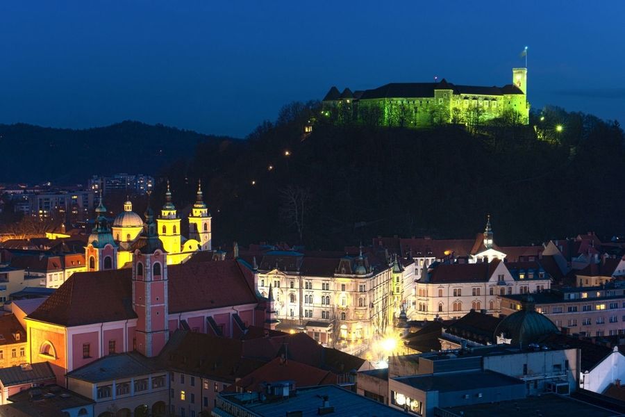 Twilight view of a European city with illuminated historical buildings, a fortress on a hill, and things to do over Easter.
