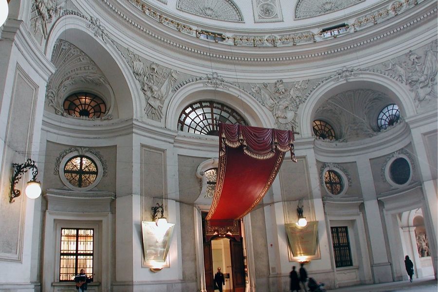 Elegant interior of a classical building featuring arched windows, intricate stucco decorations, and a large draped red banner, highlighted as one of the premier things to do in Europe over Easter.