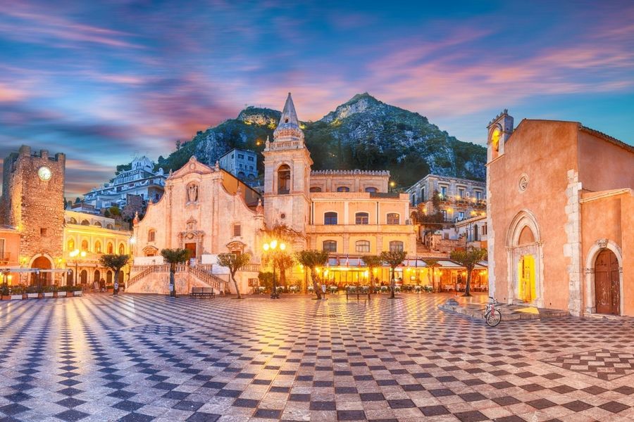 Twilight over a European square with historic architecture and a patterned pavement offers enchanting things to do in Europe over Easter.
