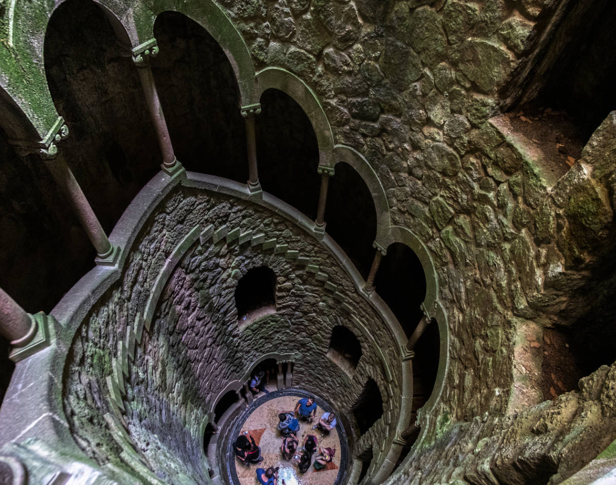 View from above of the spiral staircase of the initiation well at quinta da regaleira with visitors at the bottom.