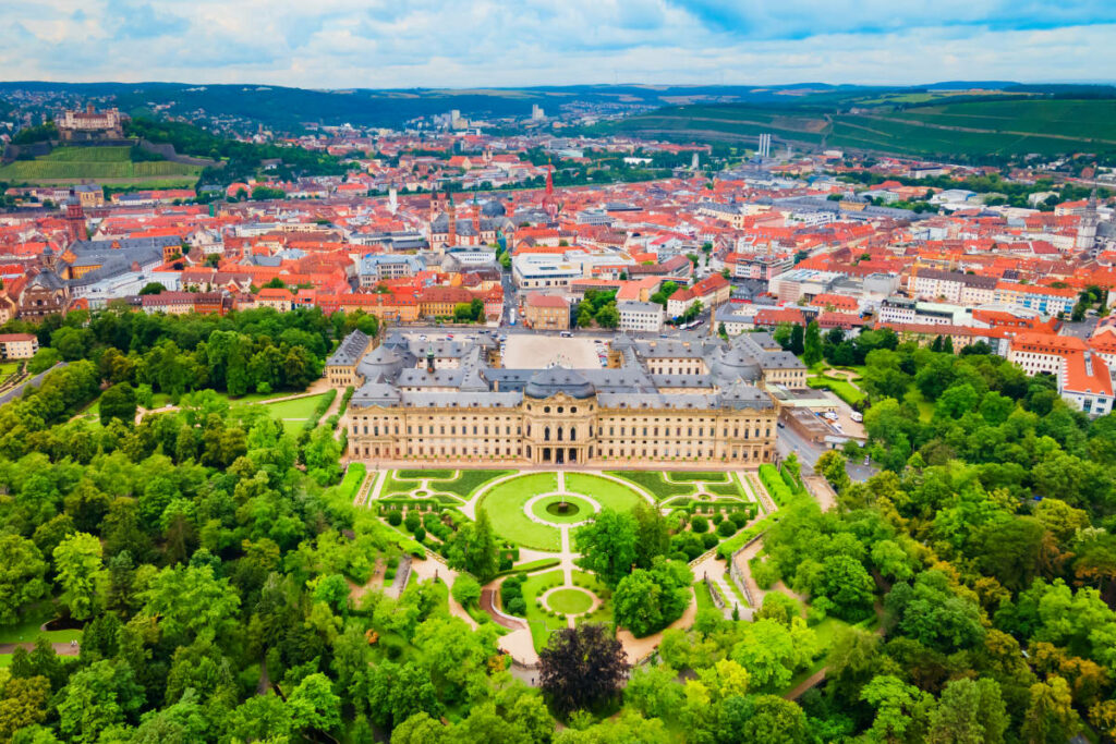 Les incontournables roadtrips européens 4 Vue aérienne de la grande résidence de Würzburg avec ses vastes jardins formels, entourée d'un paysage urbain et de collines verdoyantes sous un ciel nuageux.