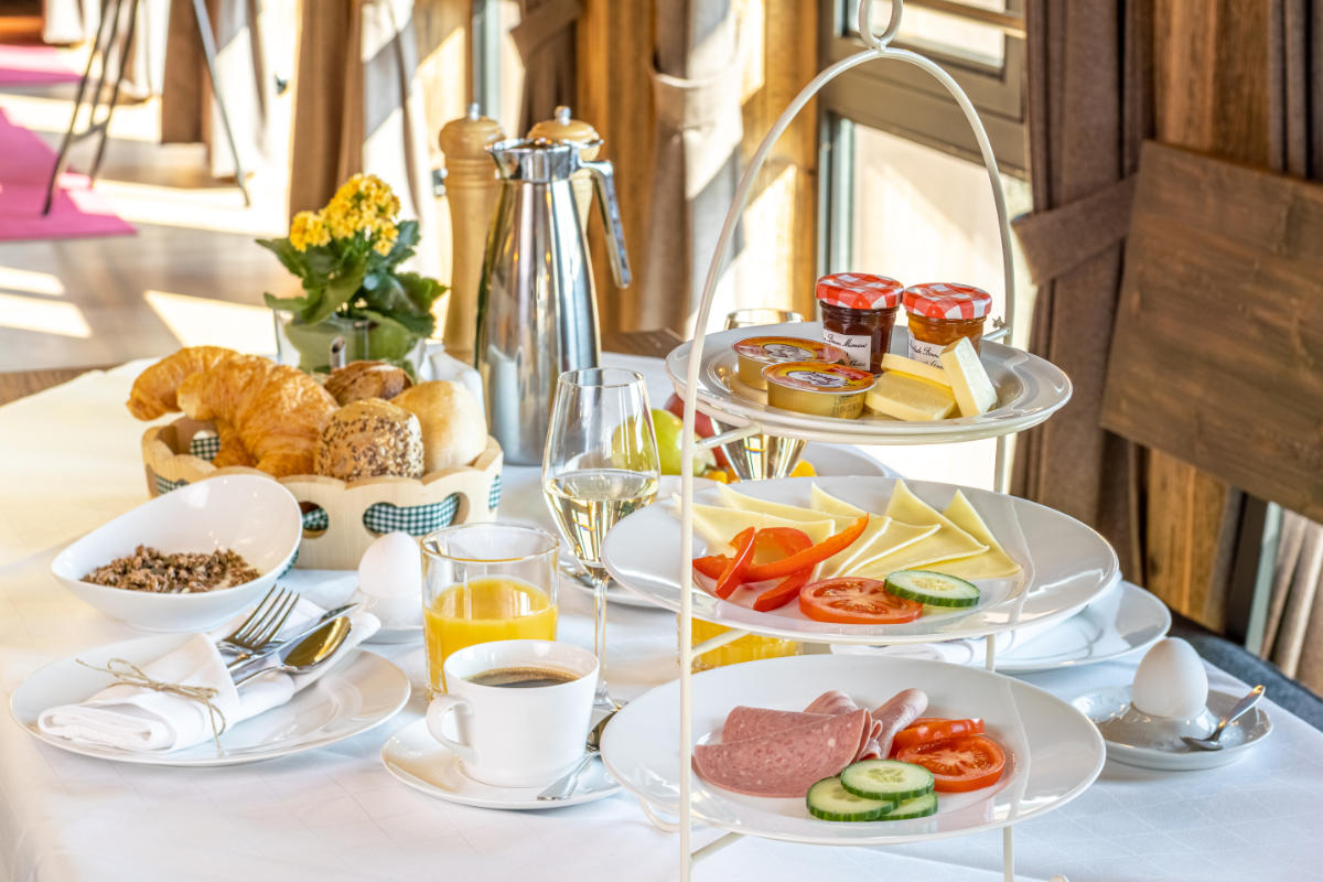Elegant breakfast setting at Schloss Frankenberg with a variety of foods on a tiered stand, including pastries and sliced fruits, complemented by coffee and juice.