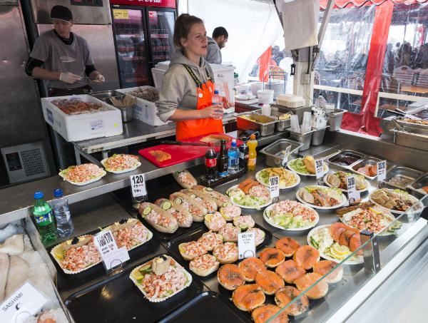 Food stall with a variety of open sandwiches on display and staff attending to customers, featured in the city guide for Bergen.