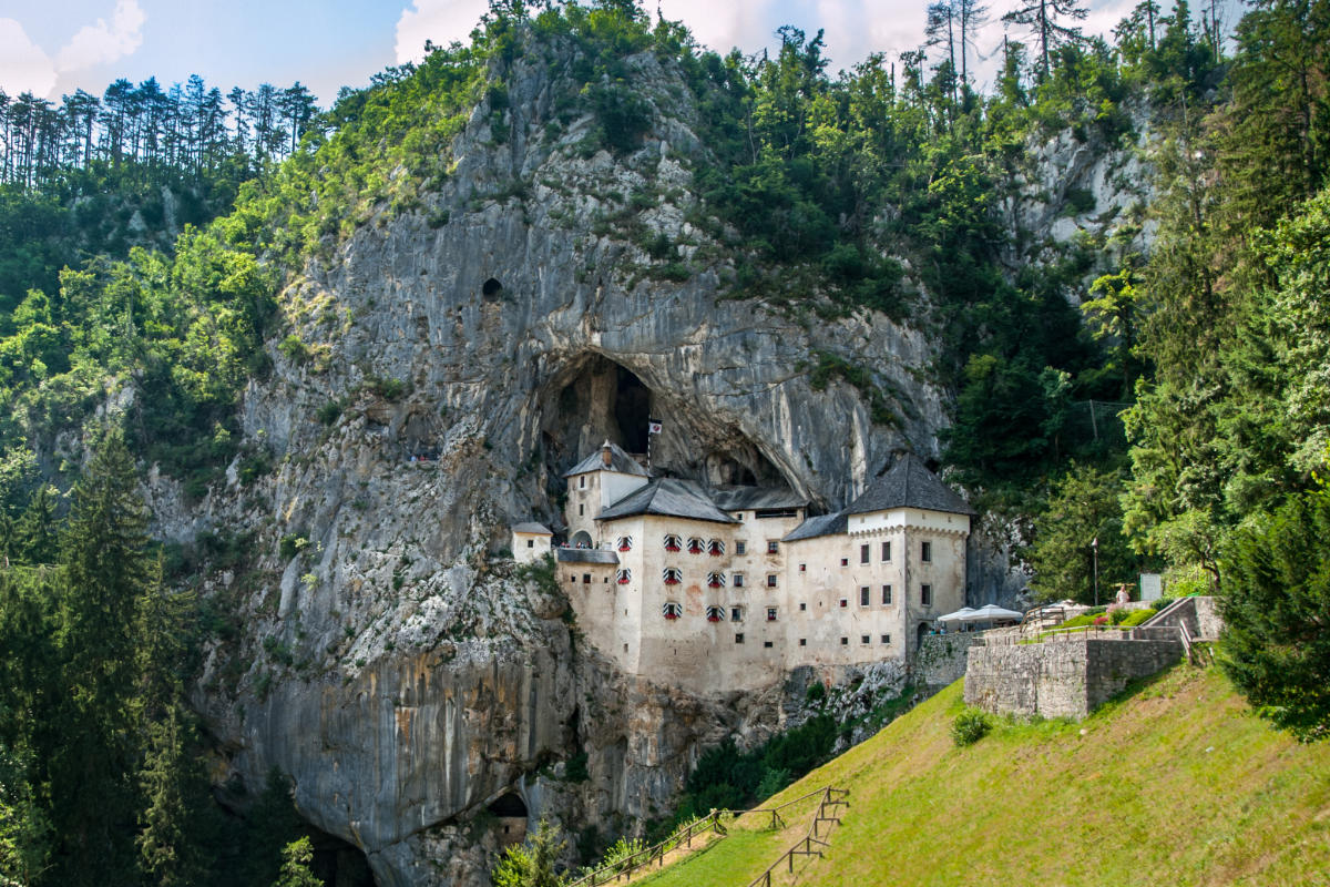 Castle built into a cave on a lush green mountainside, known as Predjama Castle, Slovenia.
