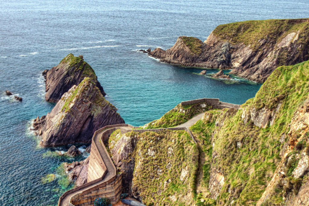 Sommer-Schnappschüsse: 6 Instagram-taugliche Orte in Europa 2 Luftaufnahme des Piers von Dunquin an den Küstenklippen mit Blick auf das türkisfarbene Wasser und die markanten Felsformationen, die ins Meer ragen.