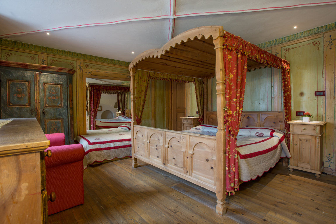 Ein Schlafzimmer mit einem hölzernen Himmelbett, roter und weißer Bettwäsche, passenden Vorhängen, antiken Möbeln und Holzböden.