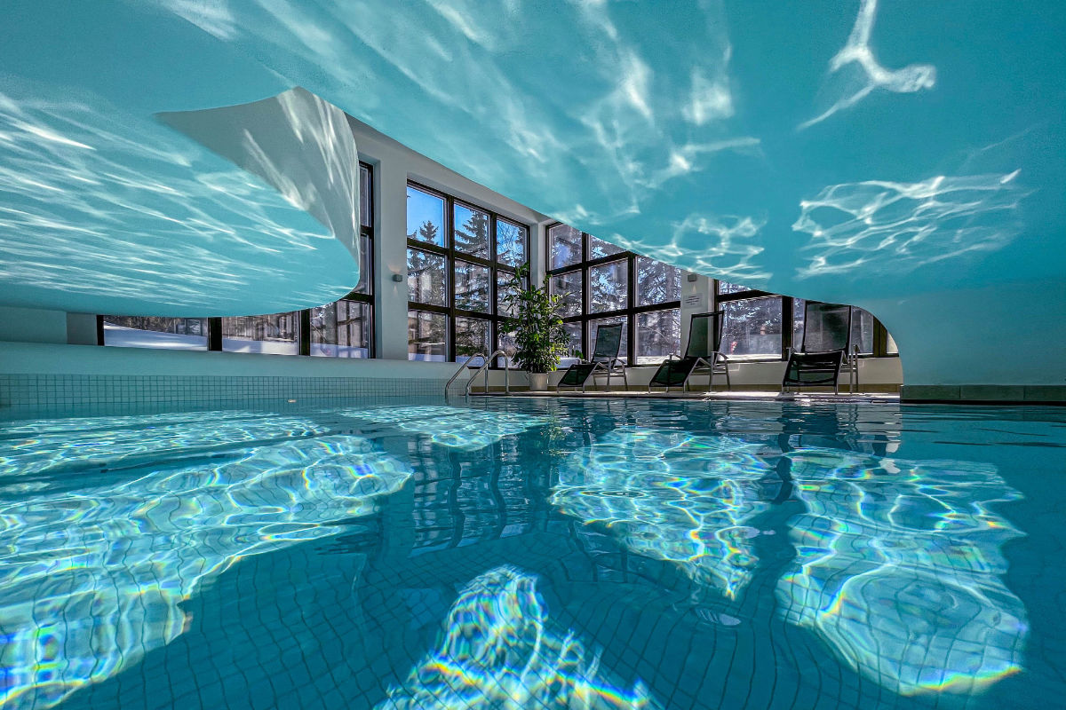 Hallenbad mit klarem, blauem Wasser, moderner Architektur und großen Fenstern, die natürliches Licht hereinlassen. Am Rande des Pools sind Liegestühle aufgestellt. Erleben Sie diesen Luxus im Cresta Palace Hotel Celerina Schweiz, einem der besten Vier-Sterne-Hotels der Schweiz.