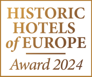 Logotipo dorado y blanco con el texto "Historic Hotels of Europe Award 2024", en honor al legado de excelencia celebrado en anteriores premios hoteleros.