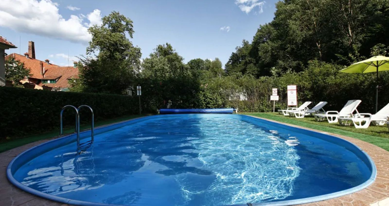 Ein Außenschwimmbad mit blauem Wasser, umgeben von Liegestühlen, Bäumen und Grünflächen an einem sonnigen Tag im Kadyny Folwark Hotel.
