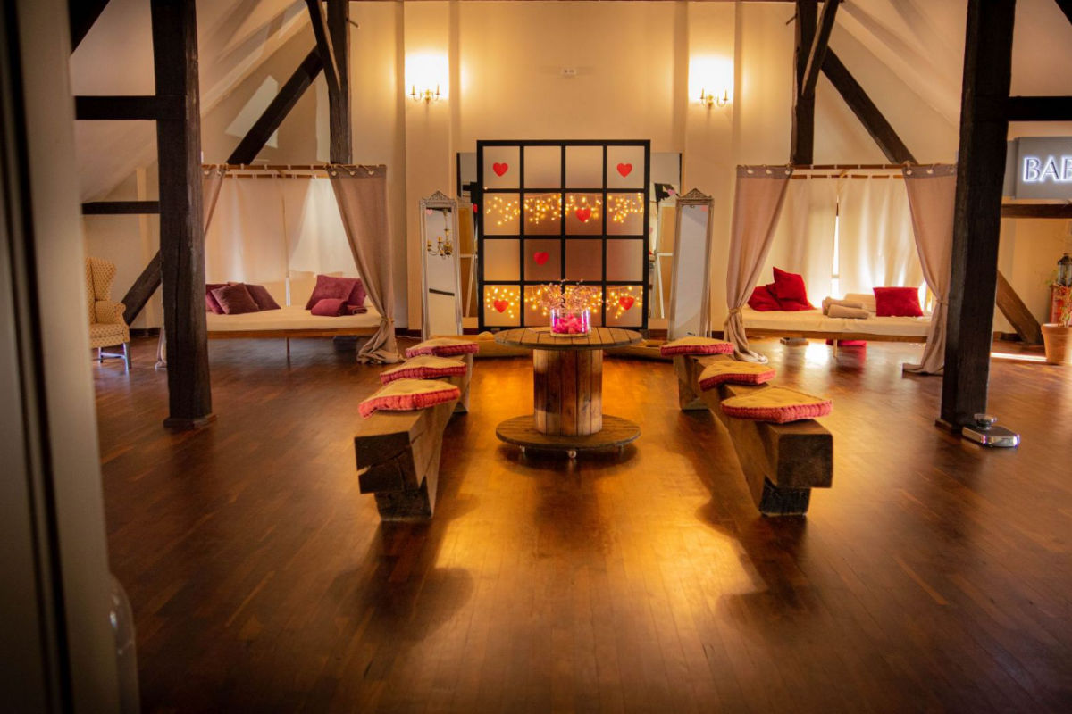 Une salle douillette et faiblement éclairée avec un sol en bois, des bancs, des lits suspendus, des coussins et une cloison décorée ornée de lumières en forme de cœur évoque le charme de Pałac Wiechlice.