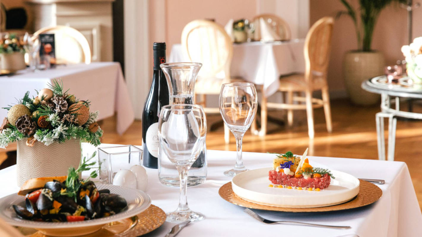 Auf einem ordentlich gedeckten Tisch im Restaurant Pałac Wojanów stehen Meeresfrüchte, elegante Gläser, eine erlesene Flasche Wein und eine exquisite Tischdekoration.