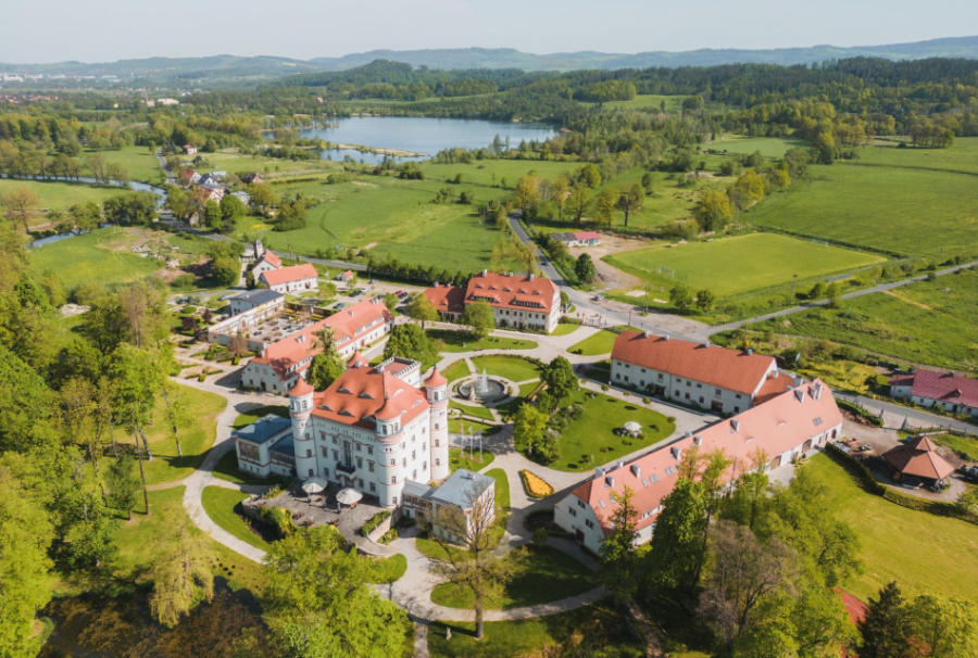 Sapori festivi: cenoni natalizi negli hotel storici 5 Veduta aerea di una tenuta di campagna con diversi edifici dai tetti rossi, inserita nel pittoresco paesaggio che circonda Pałac Wojanów, campi verdi e un lago vicino.