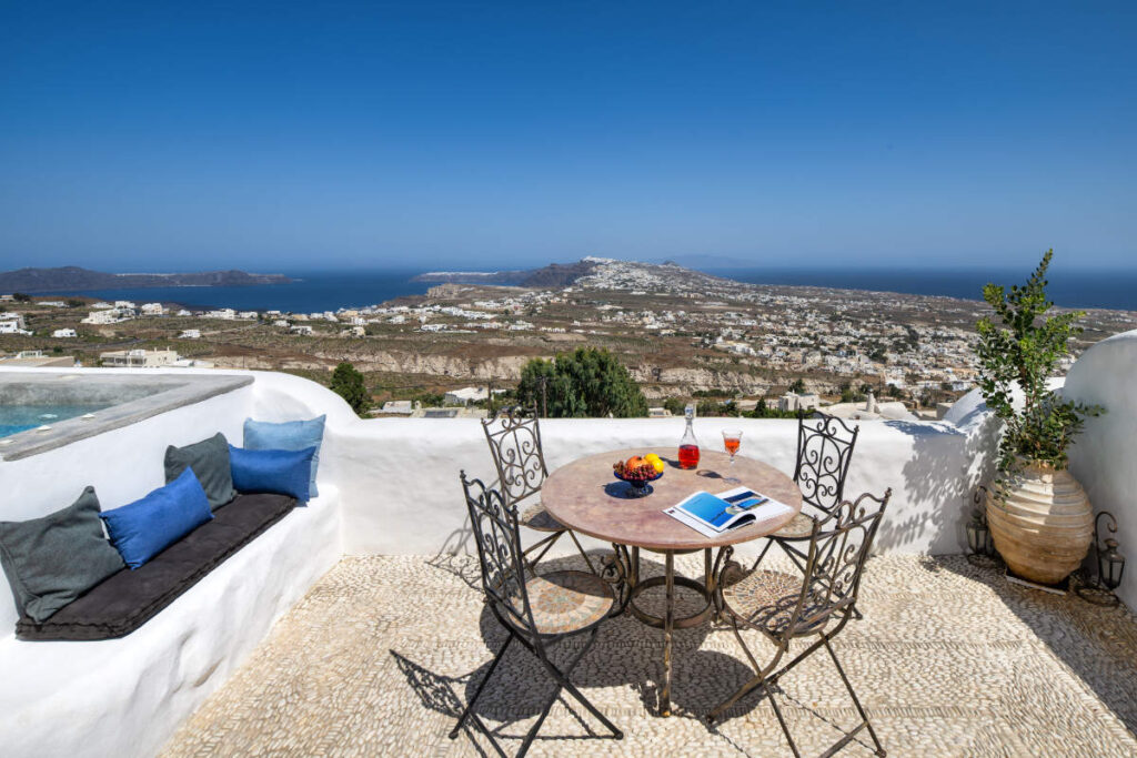 Capolavori in movimento: Le mostre d'arte da non perdere in Europa quest'estate 12 Il patio esterno di Villa Santa Croce è caratterizzato da un elegante tavolo in metallo, sedie chic e un libro accattivante. In cima si trovano bevande rinfrescanti e frutta vivace, che completano perfettamente la vista mozzafiato sul mare e sulle colline sotto il cielo azzurro di Santorini.