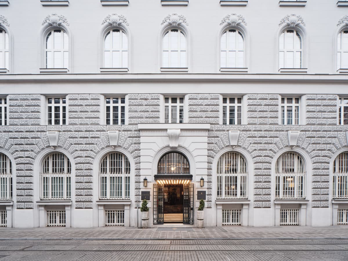 Symmetrical facade of a white, multi-story building with arched windows and a central entrance under a lit awning, epitomizing the elegant architecture found at many of the best hotels Croatia has to offer.