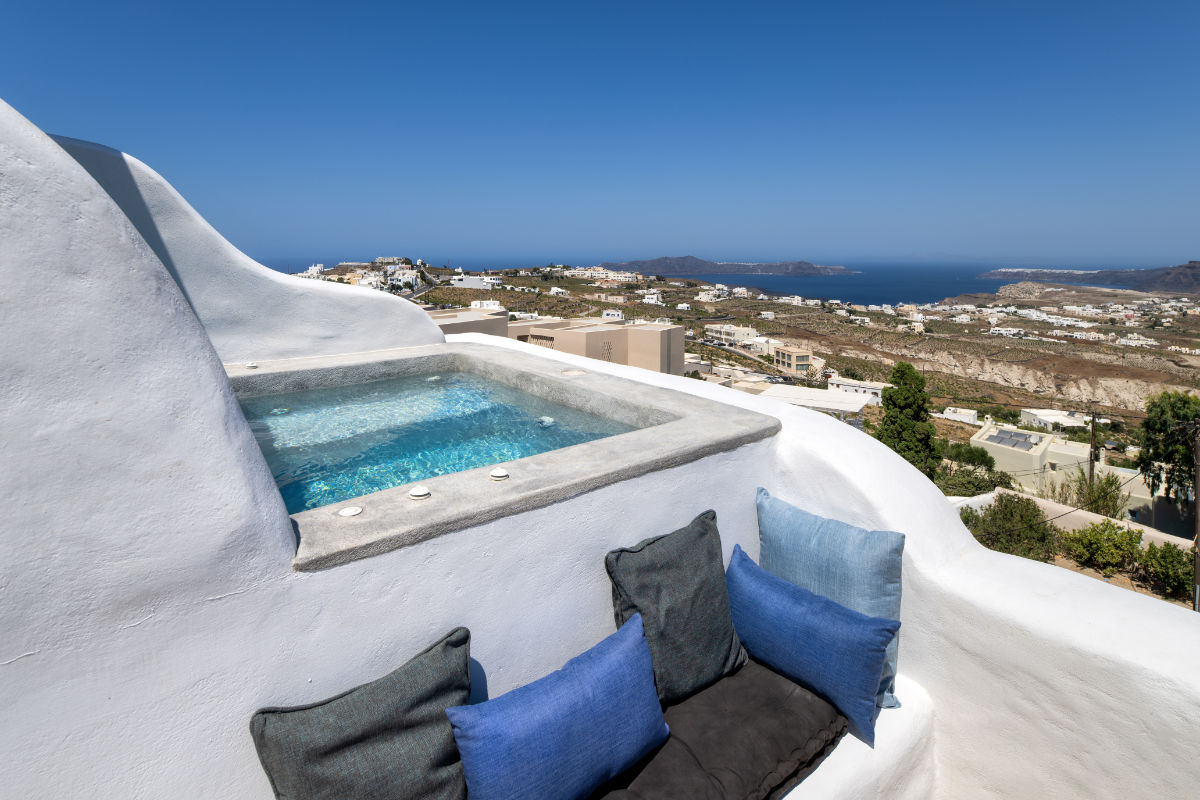 Rooftop seating area with blue and gray cushions overlooks a hillside and distant sea, featuring a small pool with clear blue water at Villa Santa Croce in Santorini.