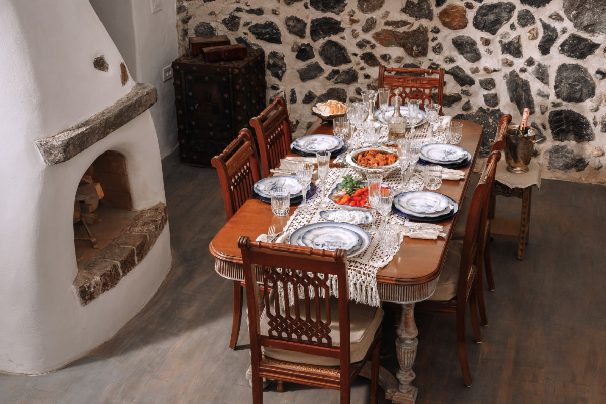 A wooden dining table set for six with plates, utensils, glasses, and a meal served is adjacent to a stone wall and a fireplace in the charming Villa Santa Croce.