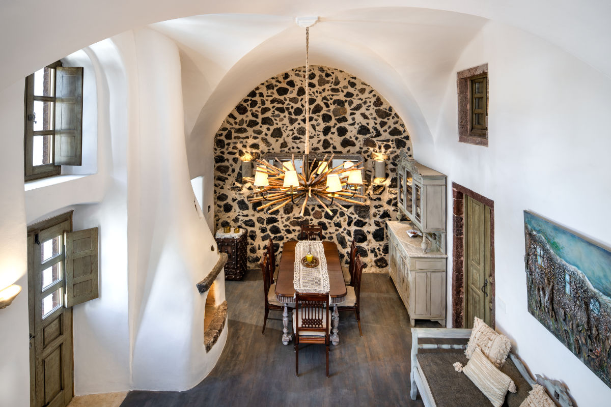 A dining room in Villa Santa Croce features white arched ceilings, a stone accent wall, wooden furniture, a large chandelier, a fireplace, and several windows.