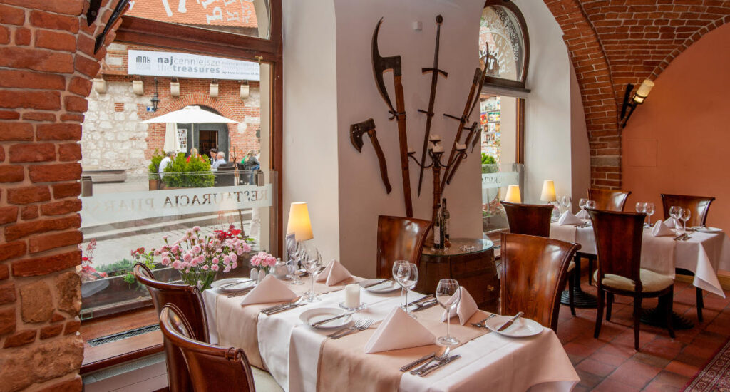 My Town : Kraków - Guide de la ville 11 Niché dans l'ambiance charmante de l'Hotel Polski, ce restaurant confortable présente des murs en briques et des fenêtres cintrées. Les tables dressées avec des nappes blanches complètent les décorations rustiques qui ornent les murs, créant ainsi une atmosphère chaleureuse et accueillante pour tous les clients.