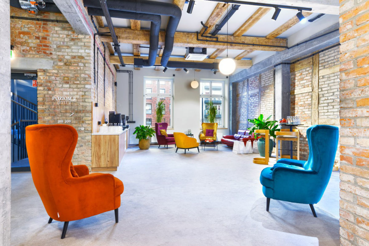 La luminosa e moderna lounge del Dwór Uphagena è caratterizzata da sedie colorate, pareti con mattoni a vista, grandi finestre, travi in legno e piante rigogliose.
