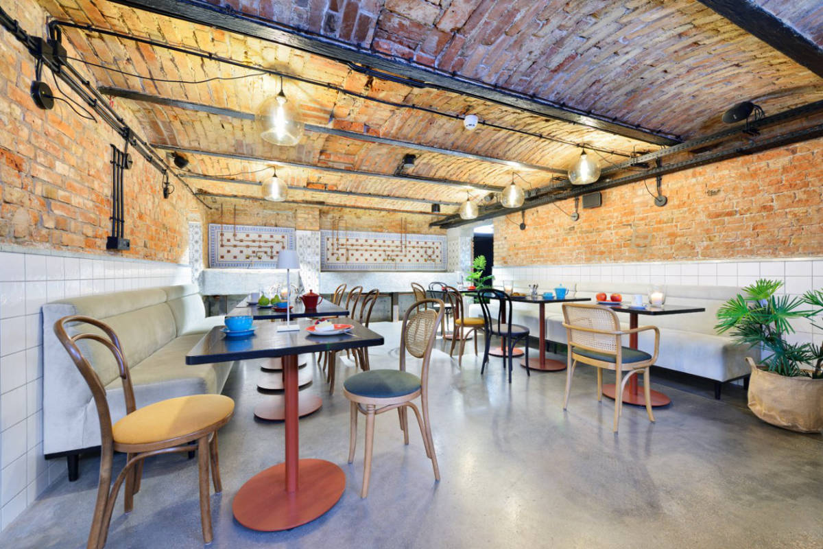 L'accogliente interno di questo caffè di Dwór Uphagena è caratterizzato da pareti in mattoni a vista e da un soffitto ad arco. Tavoli e sedie in legno sono disposti con cura e con un arredamento minimale, creando un'atmosfera calda e invitante.