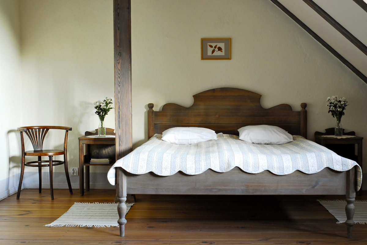 L'accogliente camera da letto del Palac i Folwark Galiny presenta un letto in legno con trapunta a righe, due cuscini e tavolini. Sulla sinistra si trovano una sedia e una piccola scrivania, ornate da vasi di fiori bianchi e completate da un quadro incorniciato alla parete.