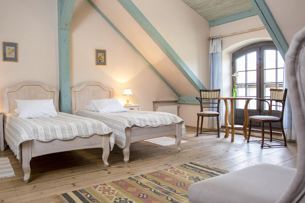 L'accogliente camera da letto in mansarda del Palac i Folwark Galiny è dotata di due letti singoli, luci soffuse e un grazioso tavolino con sedie. Una finestra ornata da tende completa gli accenti in legno e il tappeto sul pavimento in legno lucido, creando un rifugio caldo e invitante.