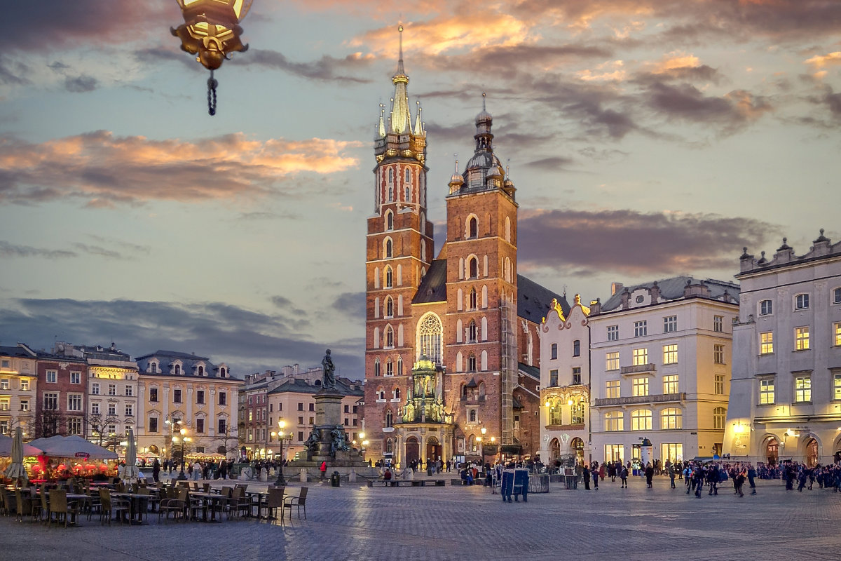 La Basilica di Santa Maria nella Piazza principale di Cracovia al tramonto, circondata da edifici storici e da un assembramento di persone.