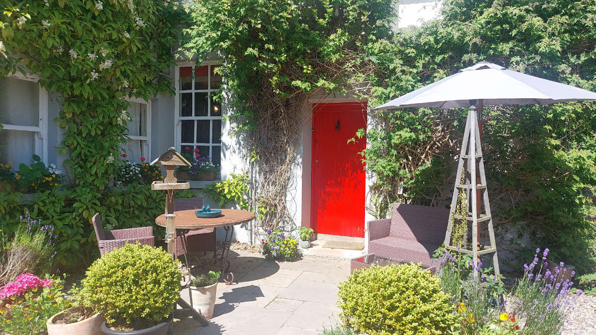 Le charmant patio du Dromore House est doté d'une porte rouge, de meubles en osier, d'une table ronde, d'un parasol et d'une végétation luxuriante.