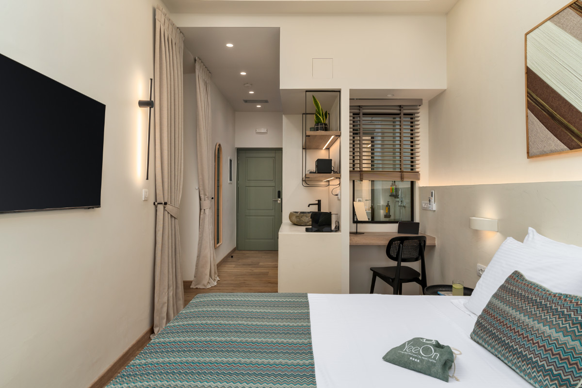 Chambre d'hôtel moderne au YeeOn Boutique Hotel de Gythio, en Grèce, avec un lit bien fait, un bureau et une chaise, une télévision à écran plat, un coin lavabo, des œuvres d'art murales et une décoration minimale dans des tons neutres.