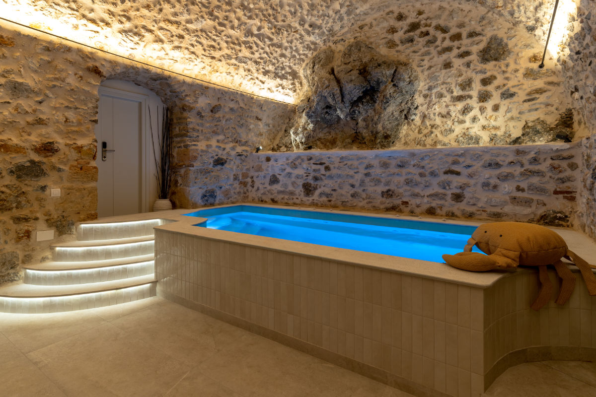 Une petite piscine intérieure à l'éclairage bleu située dans une pièce aux murs de pierre du YeeOn Boutique Hotel, avec des marches incurvées et un jouet en peluche sur le bord de la piscine.