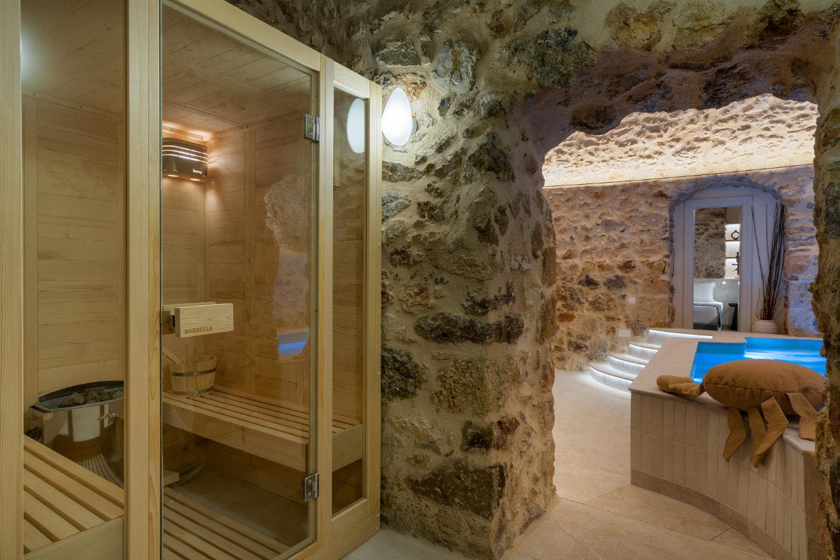 Le spa rustique aux murs de pierre du YeeOn Boutique Hotel comprend un sauna en bois sur la gauche et une petite piscine intérieure avec des marches et des serviettes sur la droite, offrant aux clients une retraite sereine dans ce charmant hôtel de Gythio, en Grèce.