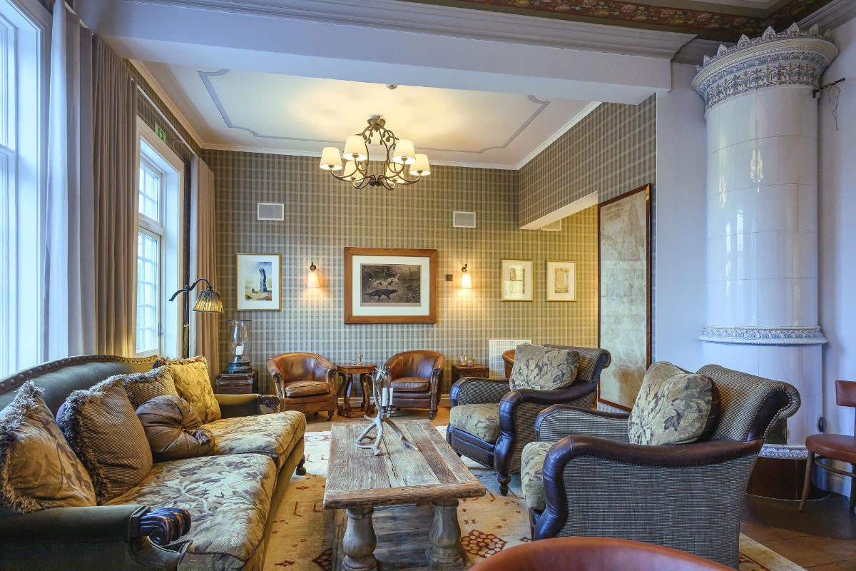 Ein traditionelles Wohnzimmer im Eriksberg Hotel mit gemusterten Tapeten, antiken Möbeln, einem Couchtisch aus Holz, gerahmter Kunst, großen Fenstern und einem weißen Keramikkamin.