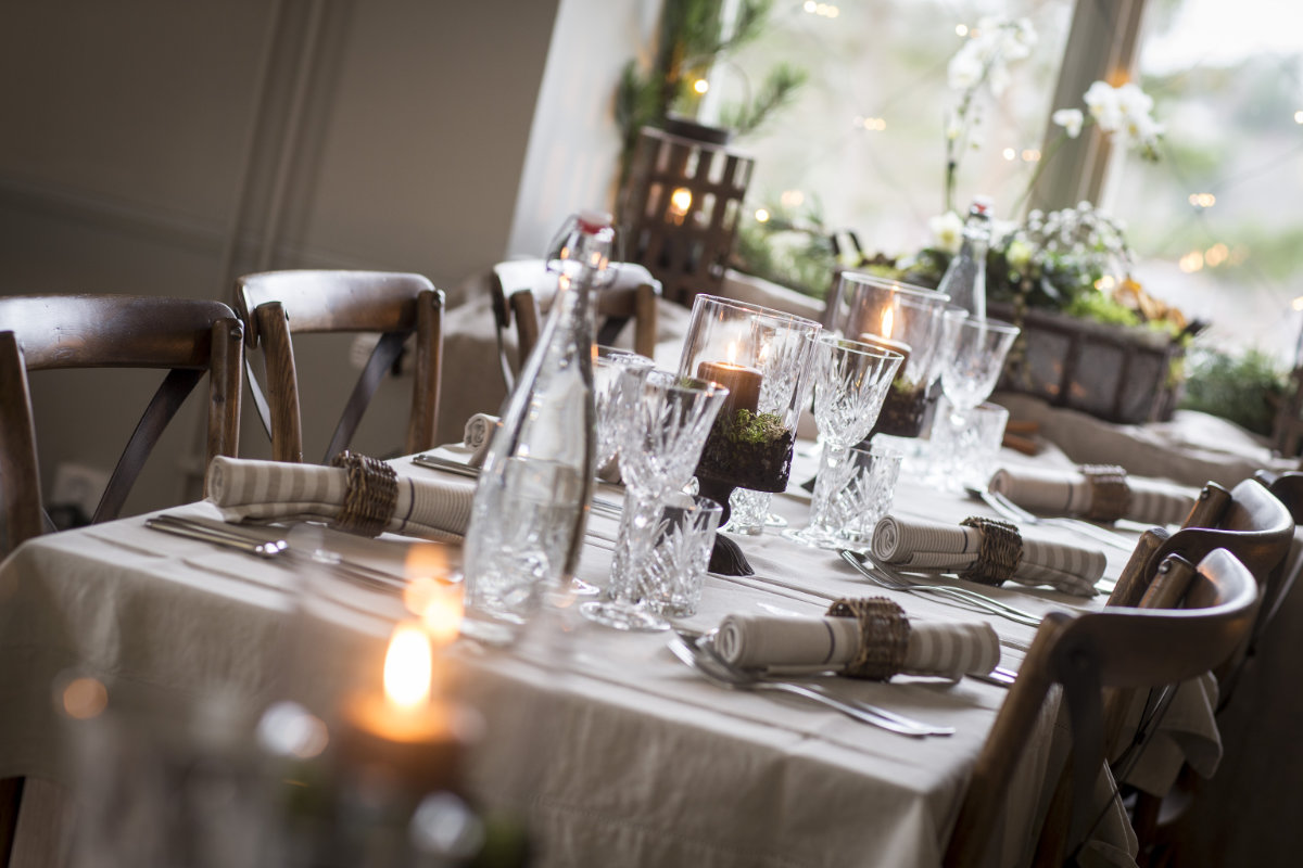 Una tavola da pranzo apparecchiata con bicchieri, candele, tovaglioli, posate e una bottiglia, disposta per un pasto in una sala decorata con luci soffuse dell'Hotel e Fortezza Fredriksborg in Svezia.