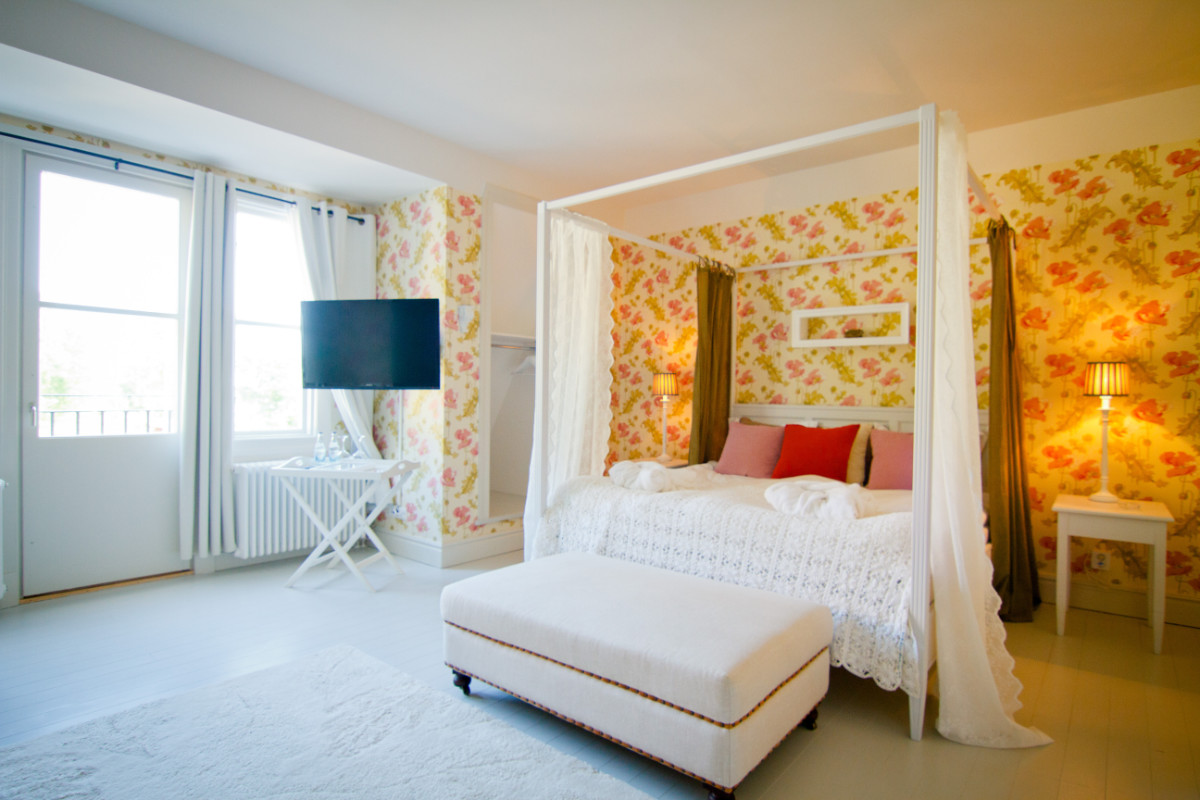 La luminosa camera da letto del Fredriksborg Hotel presenta un letto a baldacchino, una carta da parati floreale, una TV a parete, un pouf bianco e ampie finestre che lasciano entrare la luce naturale.