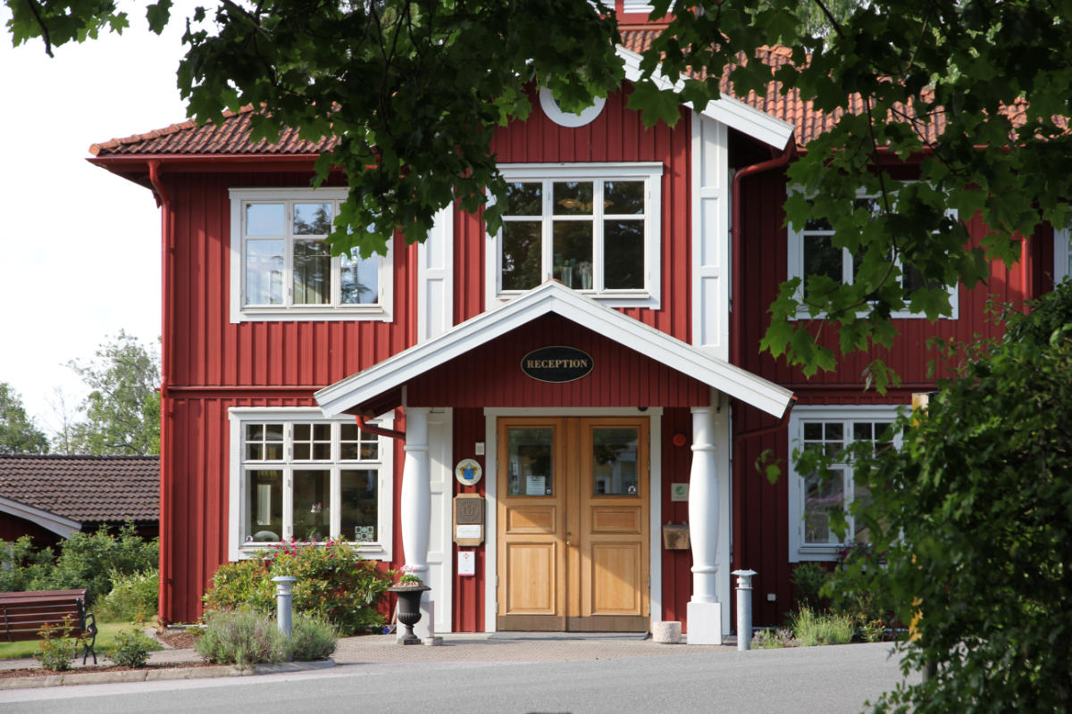 A red wooden building with white trim and a sign reading "Reception" above double doors, surrounded by greenery and trees.