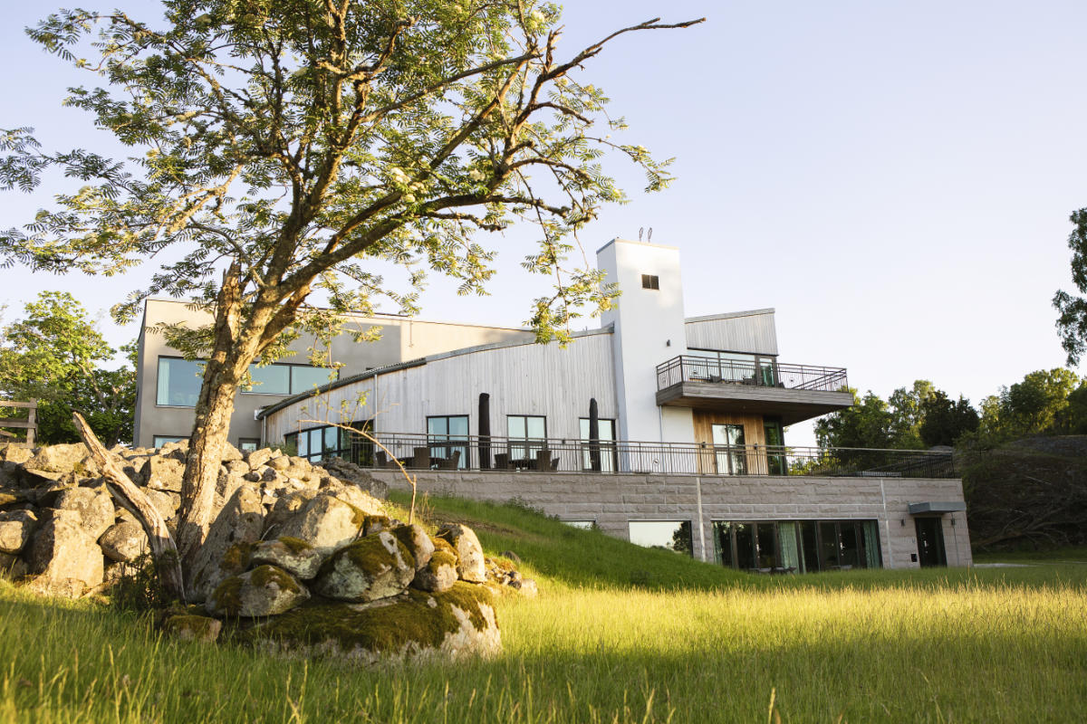 Modernes zweistöckiges Haus mit großen Fenstern und einem Balkon auf einer Rasenfläche, die an die natürliche Eleganz des Eriksberg Hotels erinnert, mit einem Baum und Felsen im Vordergrund.