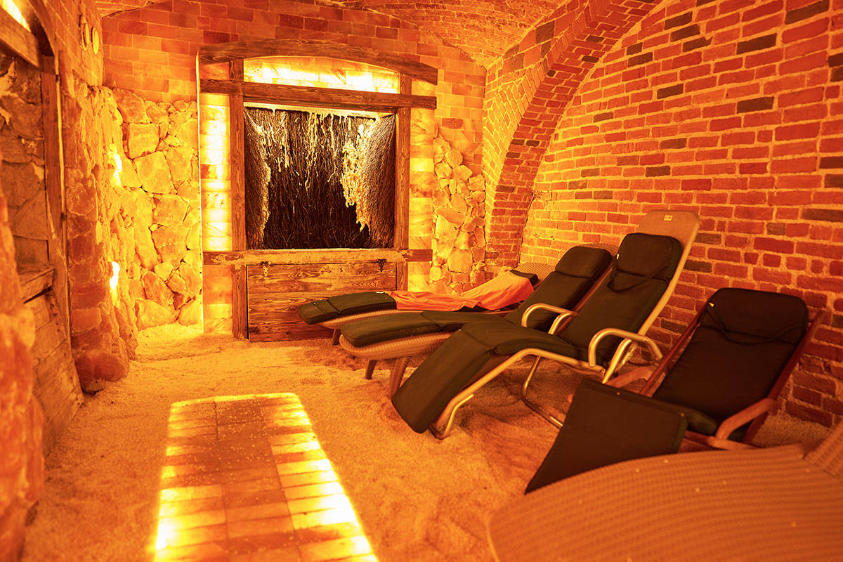 Ein Salztherapieraum mit Backsteinwänden, Liegestühlen und einem mit Salz bedeckten Boden, sanft beleuchtet mit warmem, gelbem Licht.