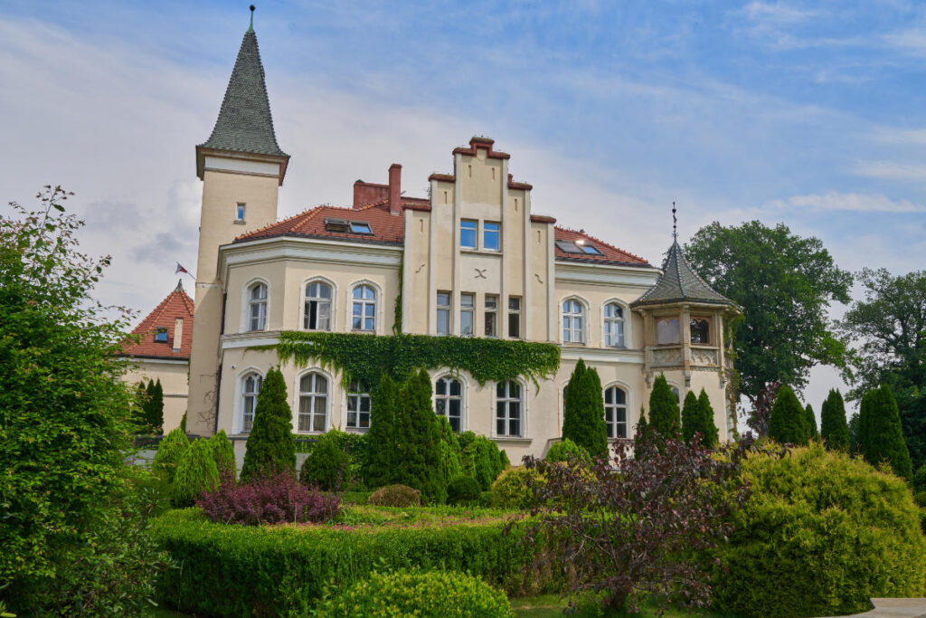L'éveil du printemps : Les jardins européens prennent vie dans le parc d'un hôtel historique 5 Grand bâtiment historique avec une tourelle, du lierre sur la façade et un jardin paysager devant, sous un ciel partiellement nuageux.