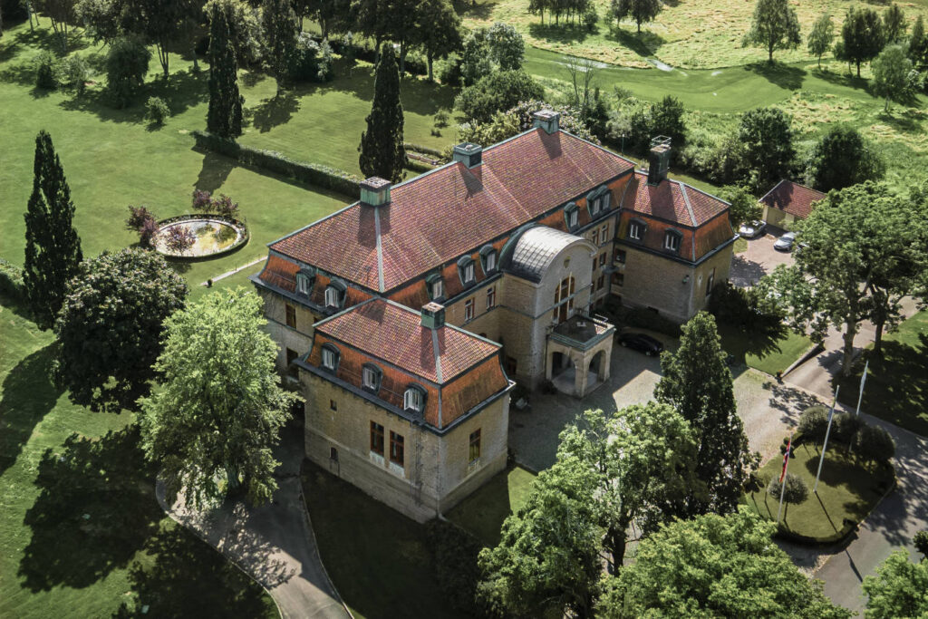 Sapori festivi: cene natalizie negli hotel storici 4 Vista aerea del castello di Bjertorp, una grande dimora storica con tetto di tegole rosse, circondata da prati verdi, alberi e giardini paesaggistici.