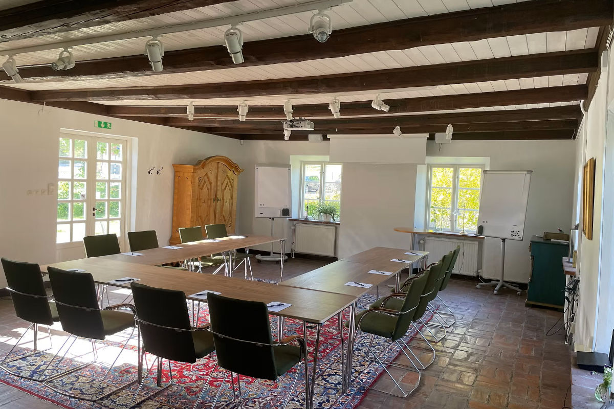 Ein Konferenzraum im Brösarps Gästgifveri & SPA ist mit U-förmigen Tischen, schwarzen Stühlen, Notizblöcken, einem Whiteboard, einem Kleiderschrank und großen Fenstern ausgestattet, die den Raum mit natürlichem Licht füllen.